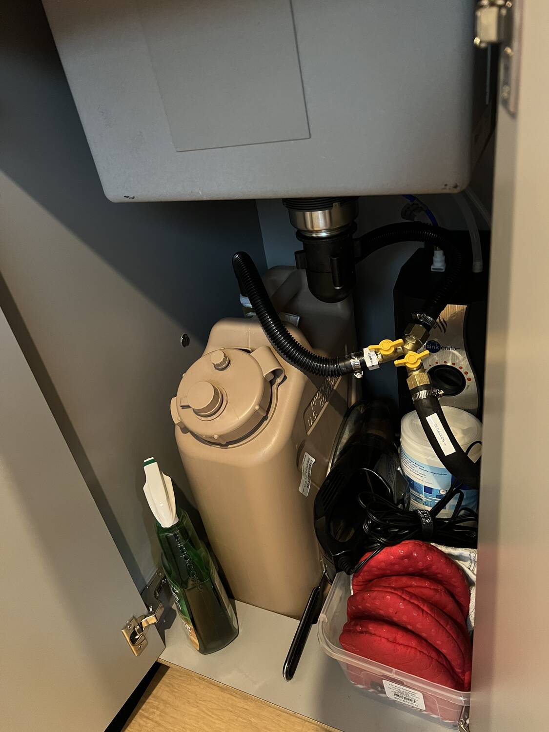 Under-sink view of the InSinkErator hot-water heater, fresh-water jug and shut-off valves