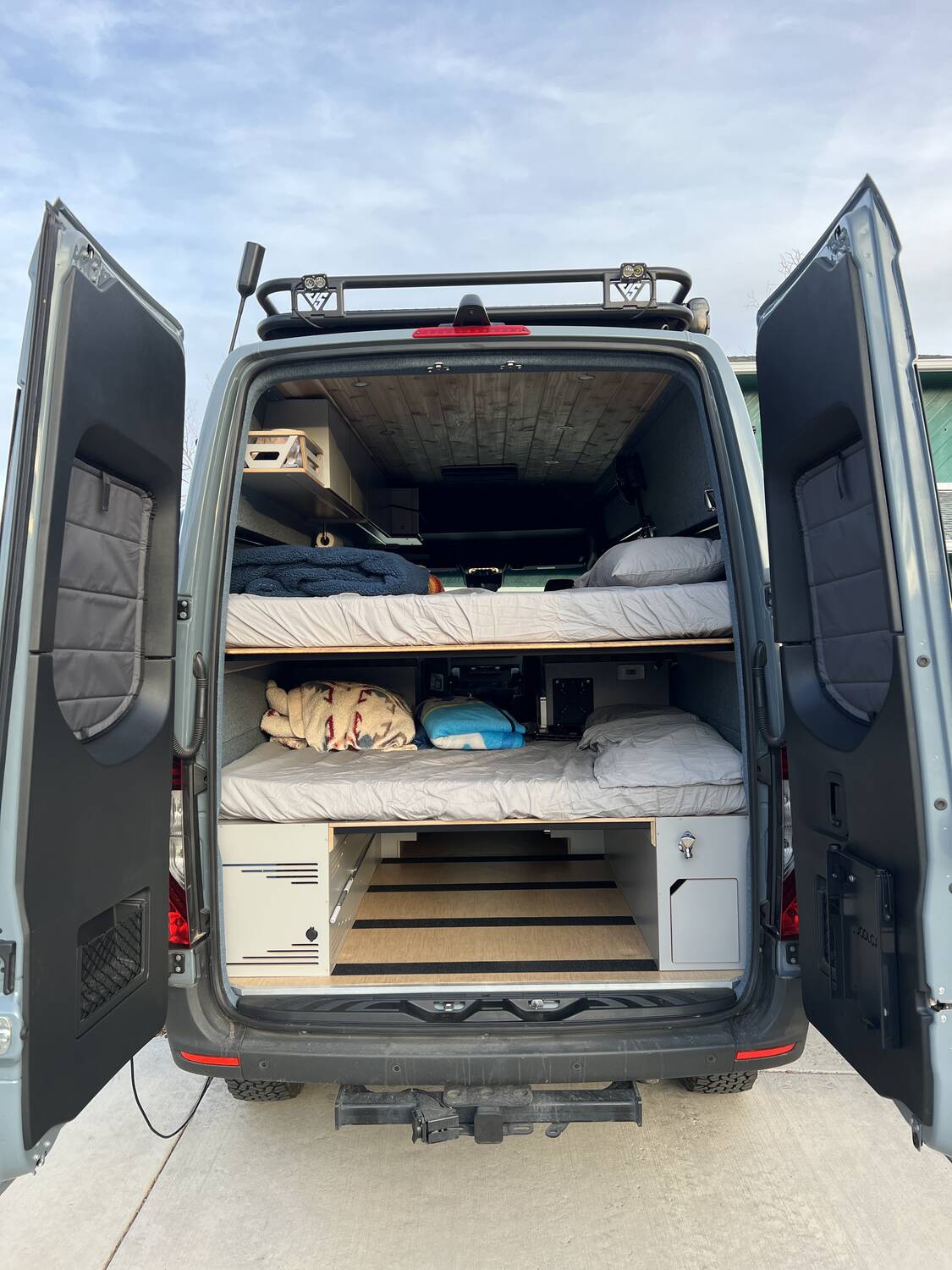 Rear doors open showing both bunks stacked with bedding and pillows