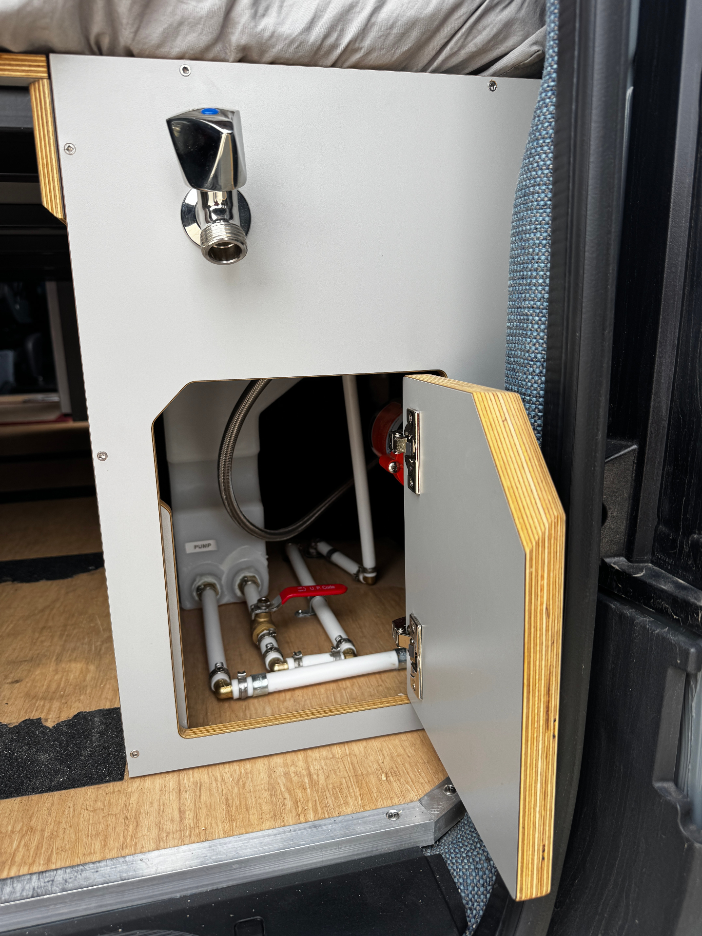 Water cabinet with access door open showing fresh-water pump, plumbing manifold and shut-off valves
