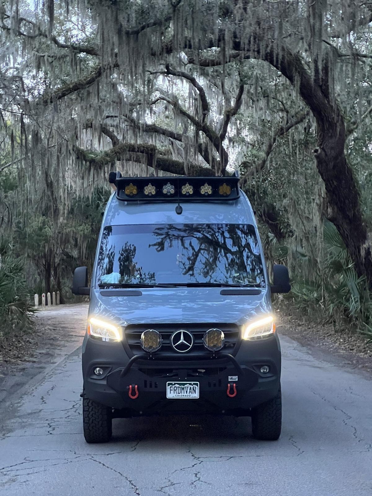 Sprinter under live oaks in the South Carolina lowcountry at dusk, headlights on