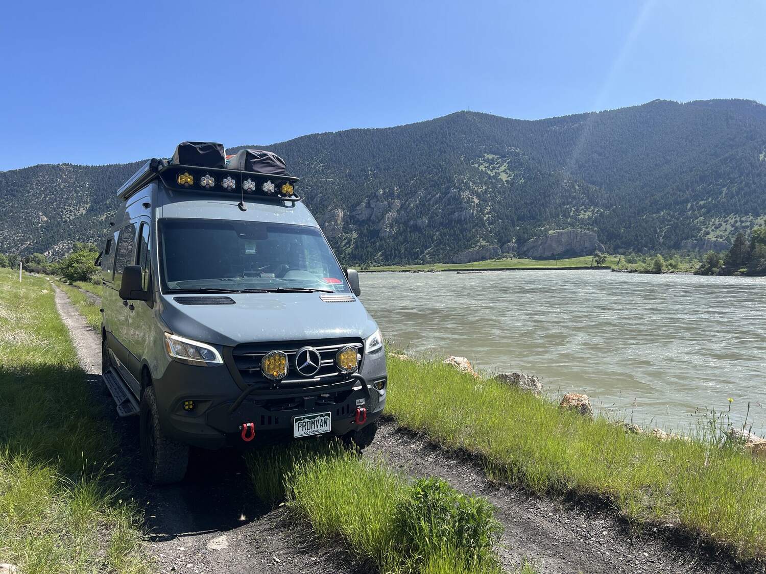 Sprinter parked beside a river with mountains beyond in Montana
